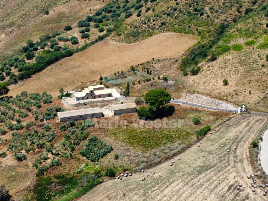 Aerial of the masseria, two barns, a fenced court, and a dry field with hay bales