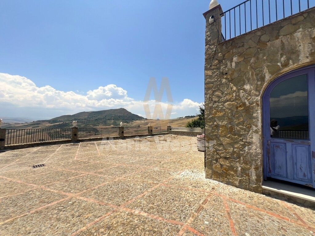 A terrace with a peeling blue door and hills beyond the rail