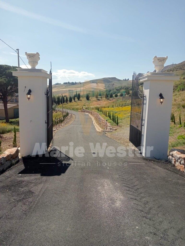 An open iron gate between white pillars, and a new drive into the hills