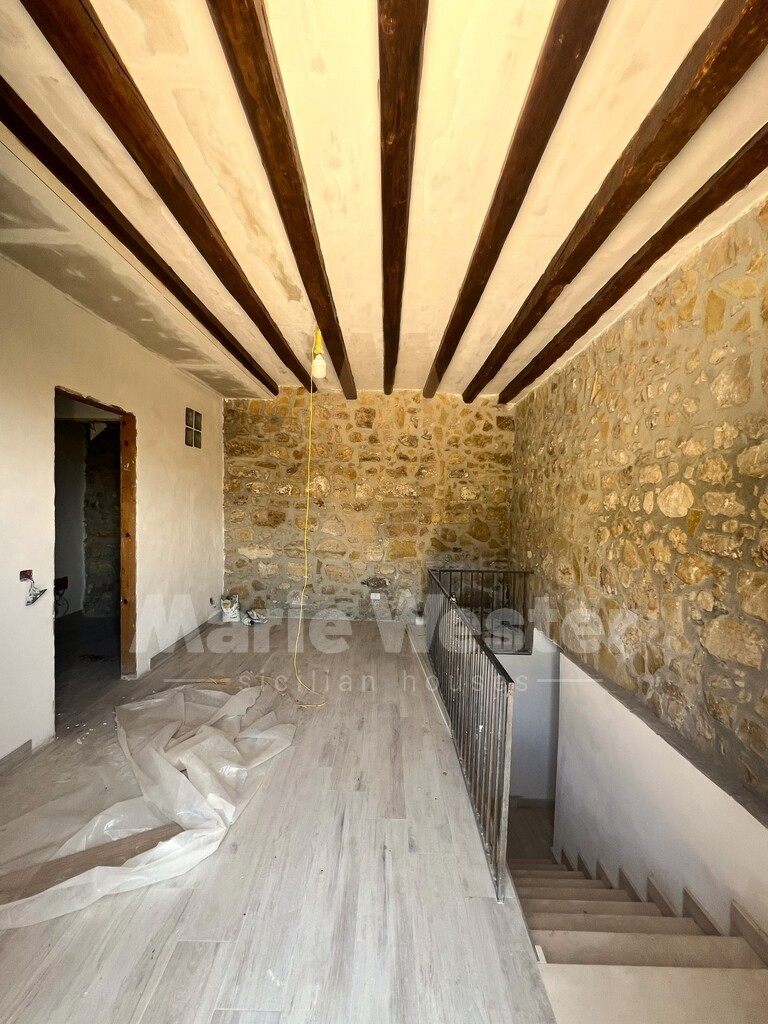 An unfinished upper room with a bare stone wall, a hanging bulb, and plastic on the floor