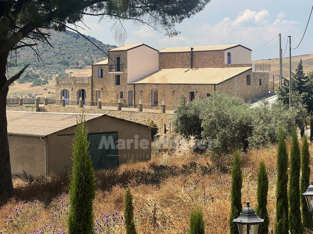 The stone masseria seen across dry grass, with a shed in front and hills behind