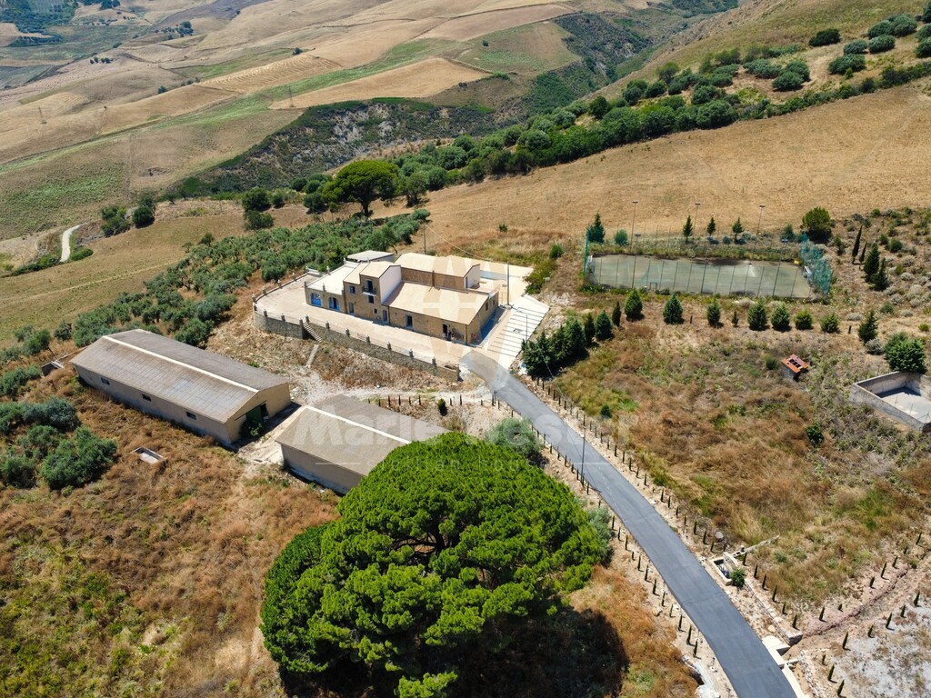 Aerial of the stone masseria, two long barns, a fenced tennis court, and dry hills