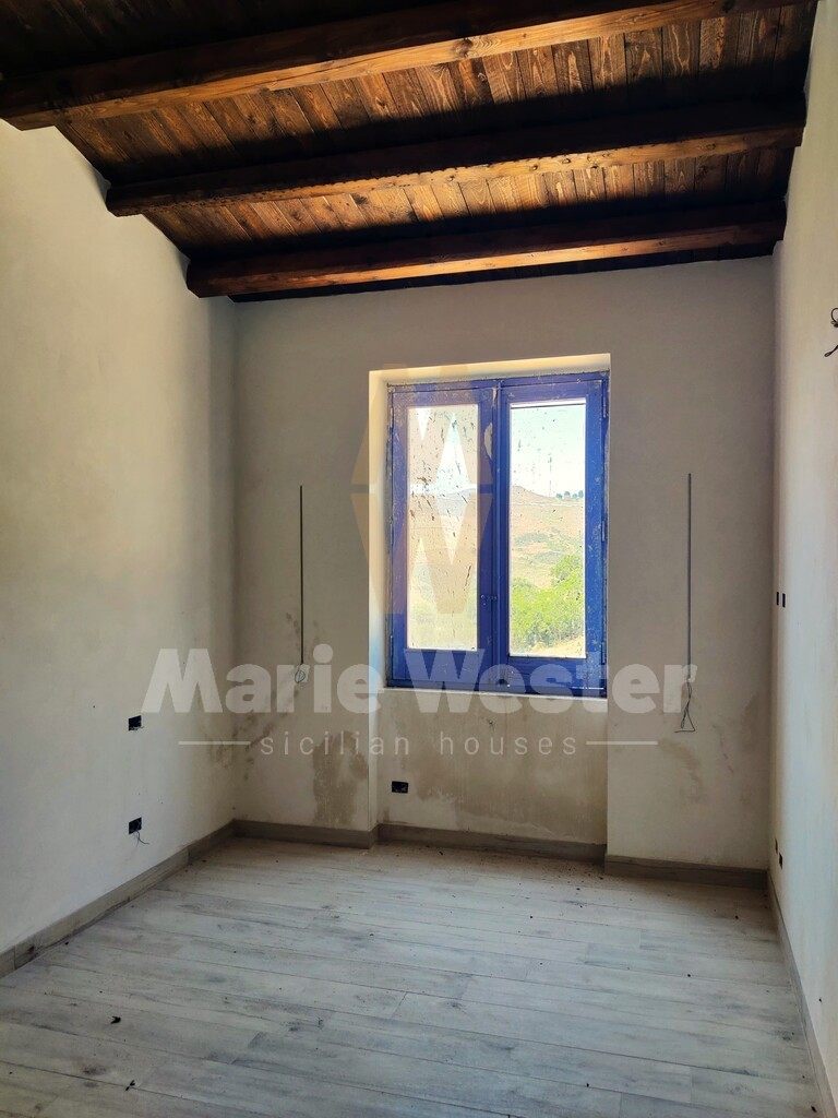 An empty room with patched plaster, a worn blue window, and hills outside