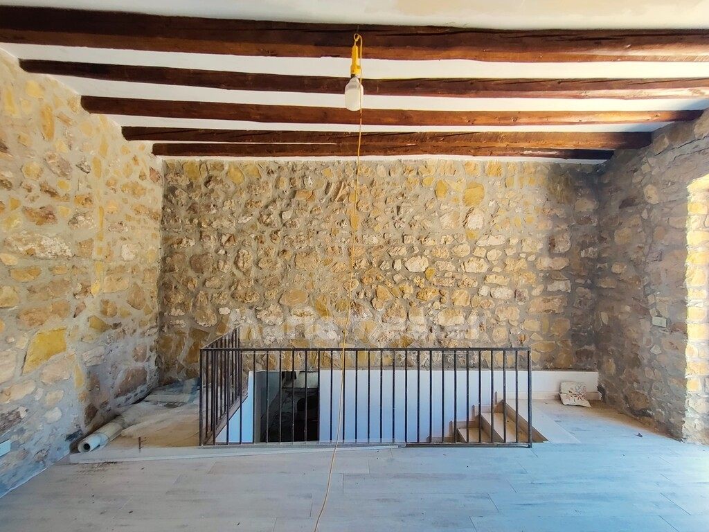 A stone room with wooden beams and an open stairwell guarded by a black rail