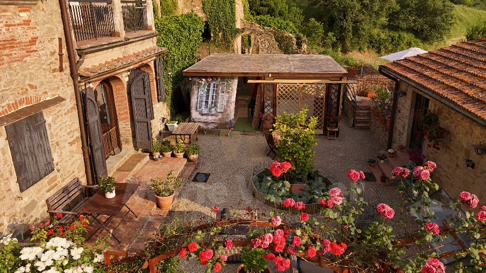 A stone courtyard in Lamole with roses, shutters, and a small summer kitchen