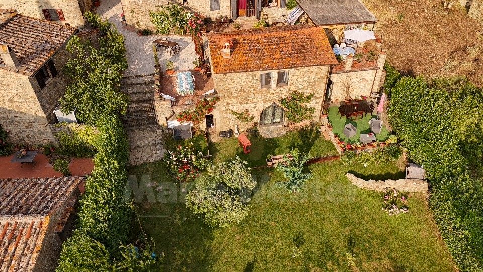 Aerial of one stone house and a walled garden, with neighbouring roofs tight on the left