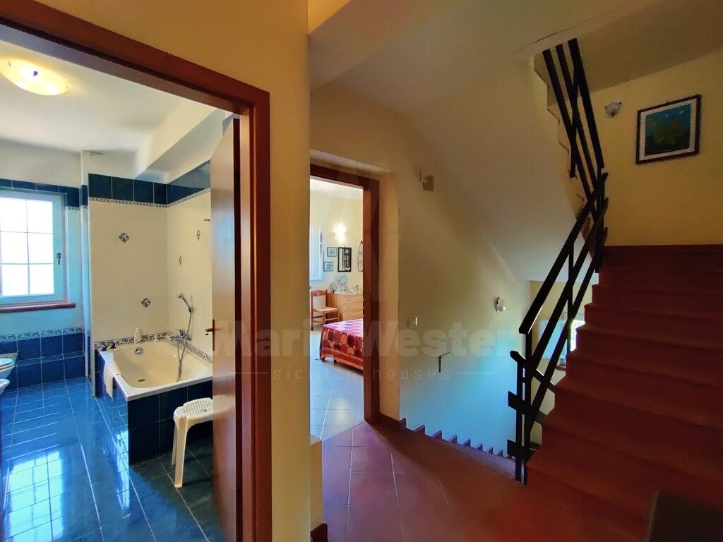 A blue-tiled bathroom beside a wooden stair, with a bedroom visible beyond