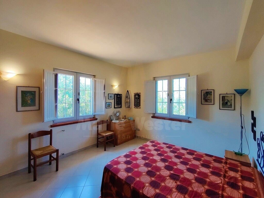 A bedroom with open white shutters and a red patterned cover
