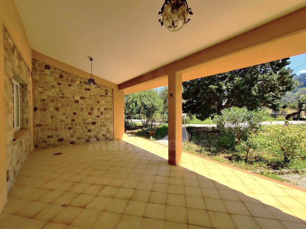 An empty covered loggia with yellow floor tiles and a stone wall