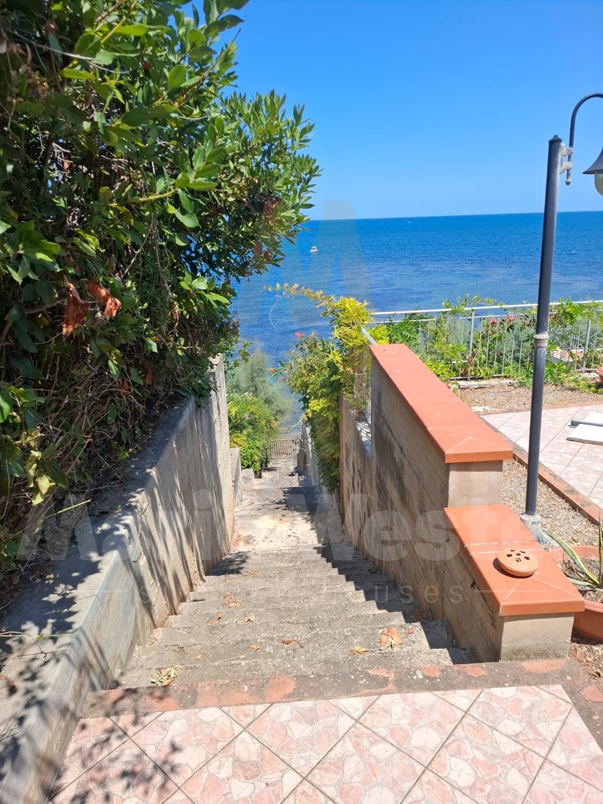 A concrete stair leaving a tiled terrace and descending toward the sea