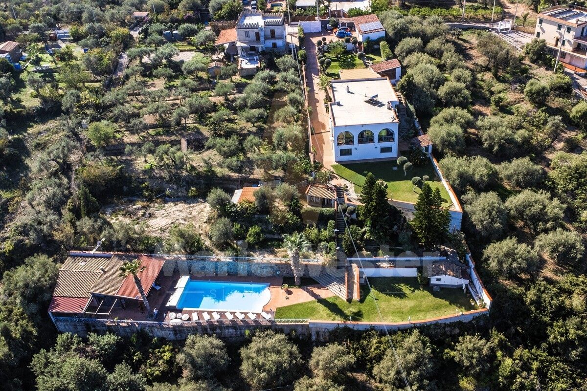 Closer aerial of the drive, the white house, and the pool at the bottom of the frame