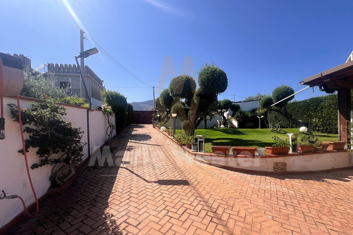 A brick drive through clipped trees and lawn, with mountains beyond