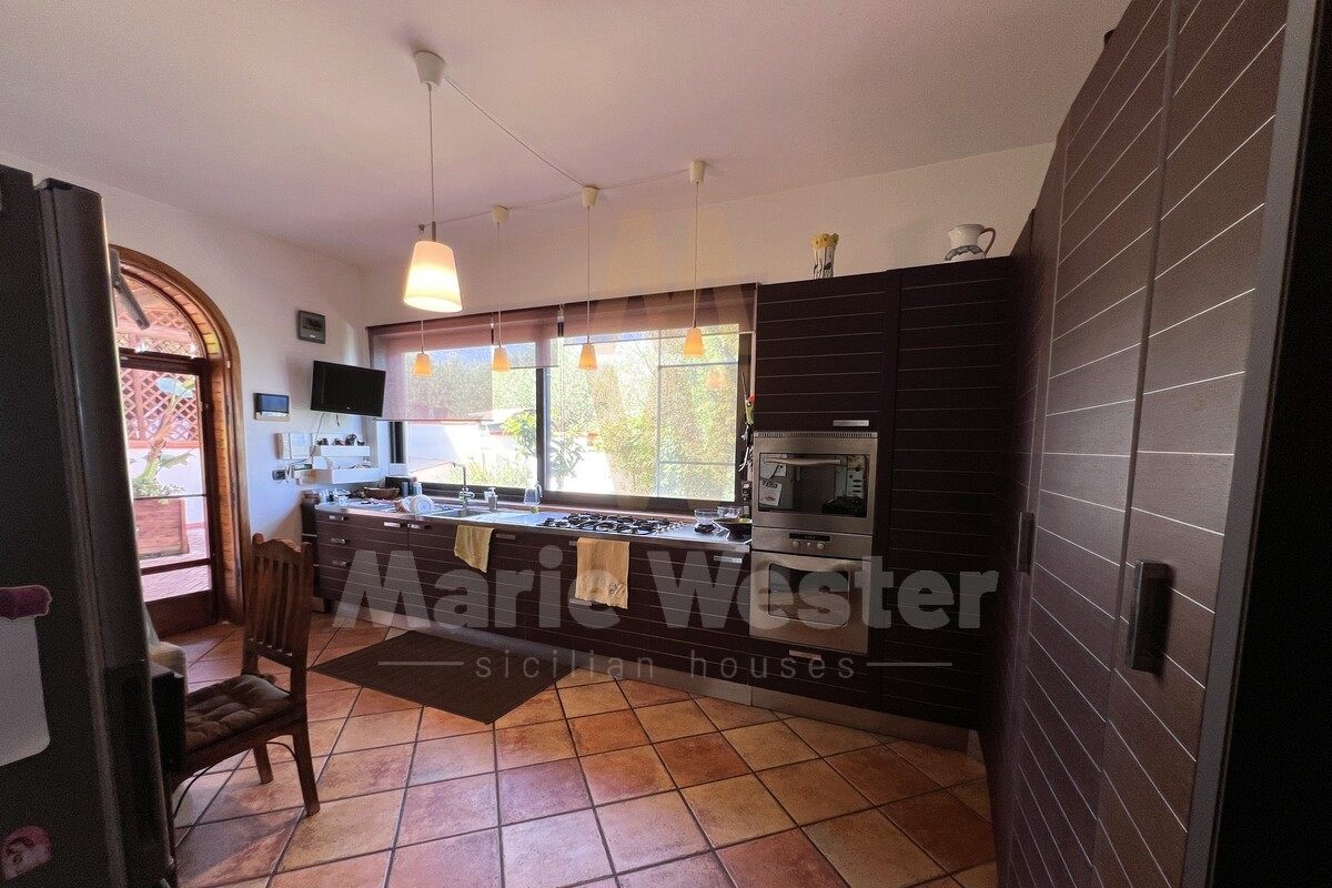 A dark modern kitchen with an arched door open to a terrace