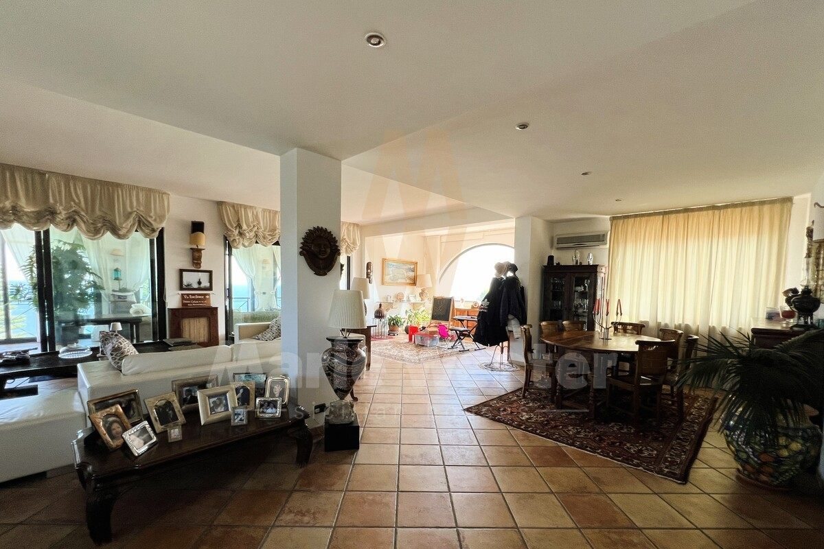 A large living and dining room with the sea visible through the windows and family photographs on a surface
