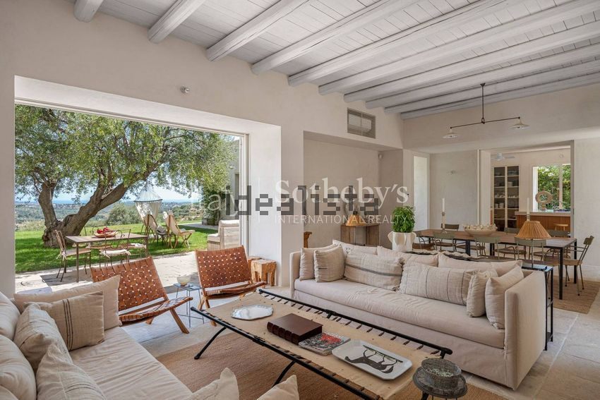 A furnished sitting room opening onto a terrace, with a dining table further inside