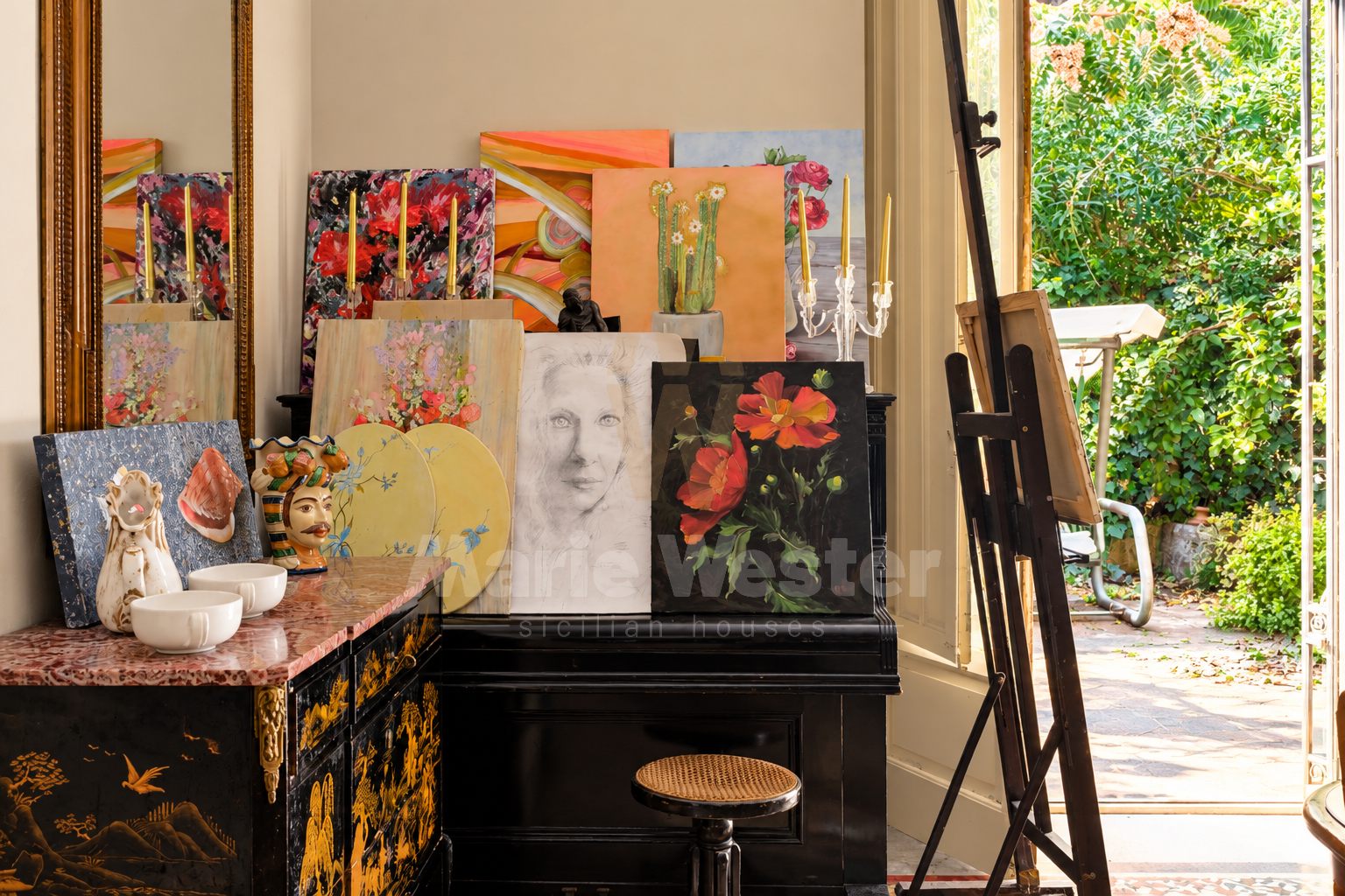 A piano and stacked paintings beside a door open to the garden