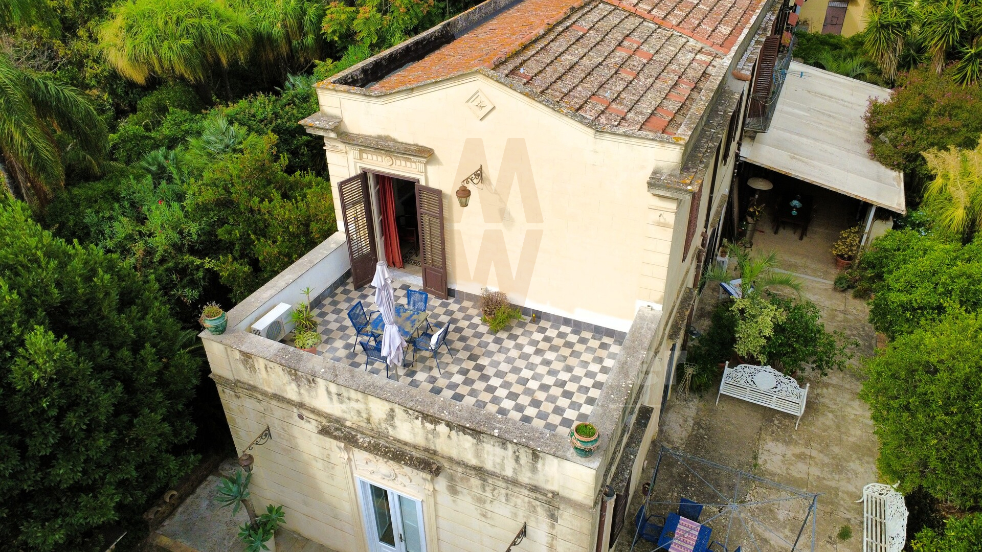 The cream villa from above, a checkered roof terrace and the garden around it