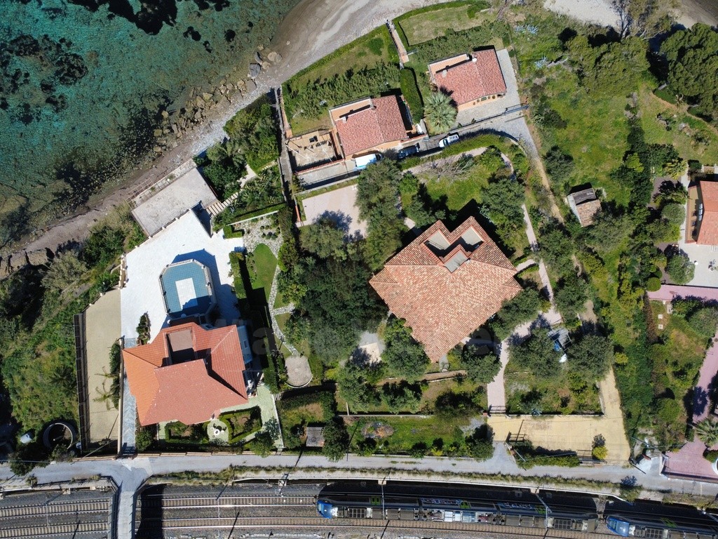 Overhead view of the tiled roofs, the shore, and a train on the tracks behind the property