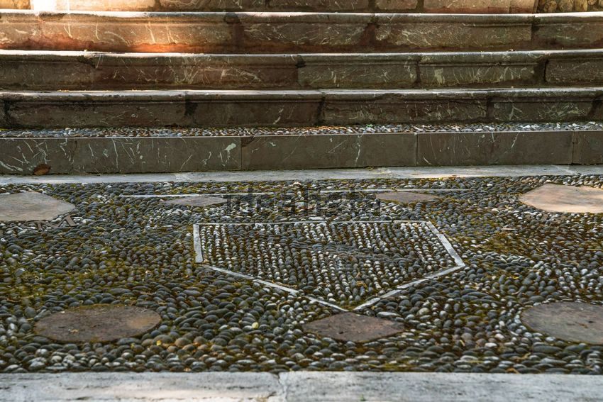 Black and white pebble paving in a shield pattern at the foot of marble steps