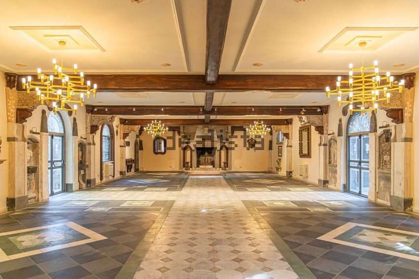 A long empty hall with chandeliers, a patterned stone floor, and carved stone pieces in wall niches