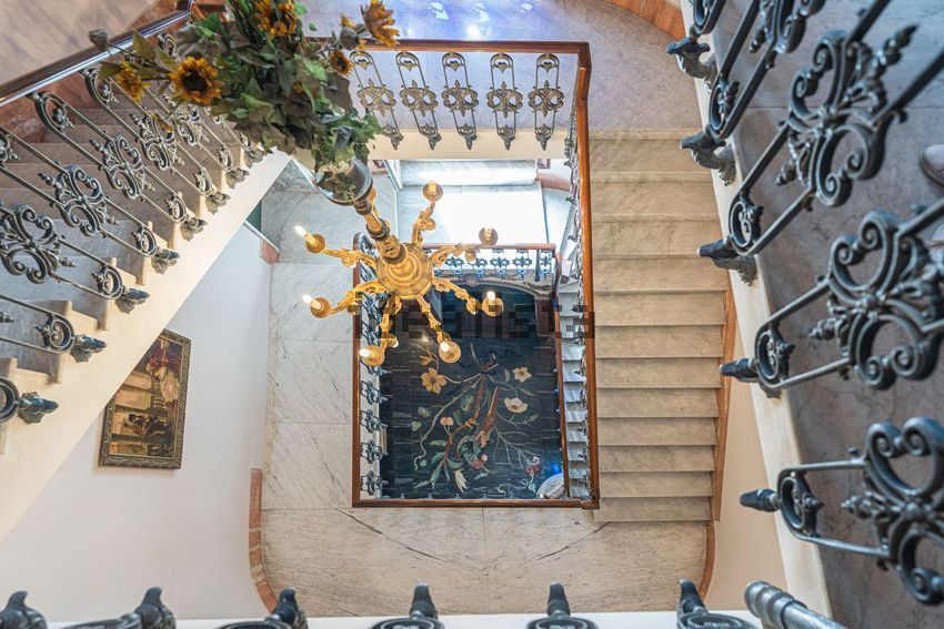 A marble staircase with an iron rail, a chandelier, and a floral tile floor seen from above