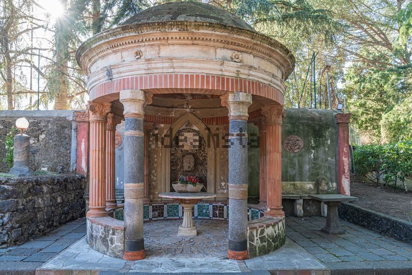 A round open temple with columns and a stone basin, set in the garden
